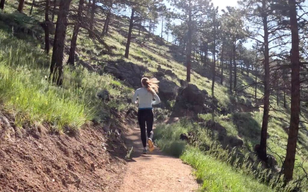 Dr. Chloe trail running through a wooded area on a sunny day